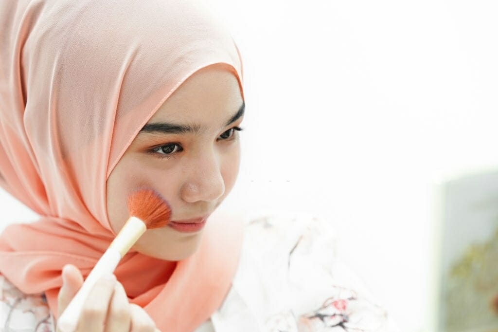 young muslim woman with mirror and makeup brush