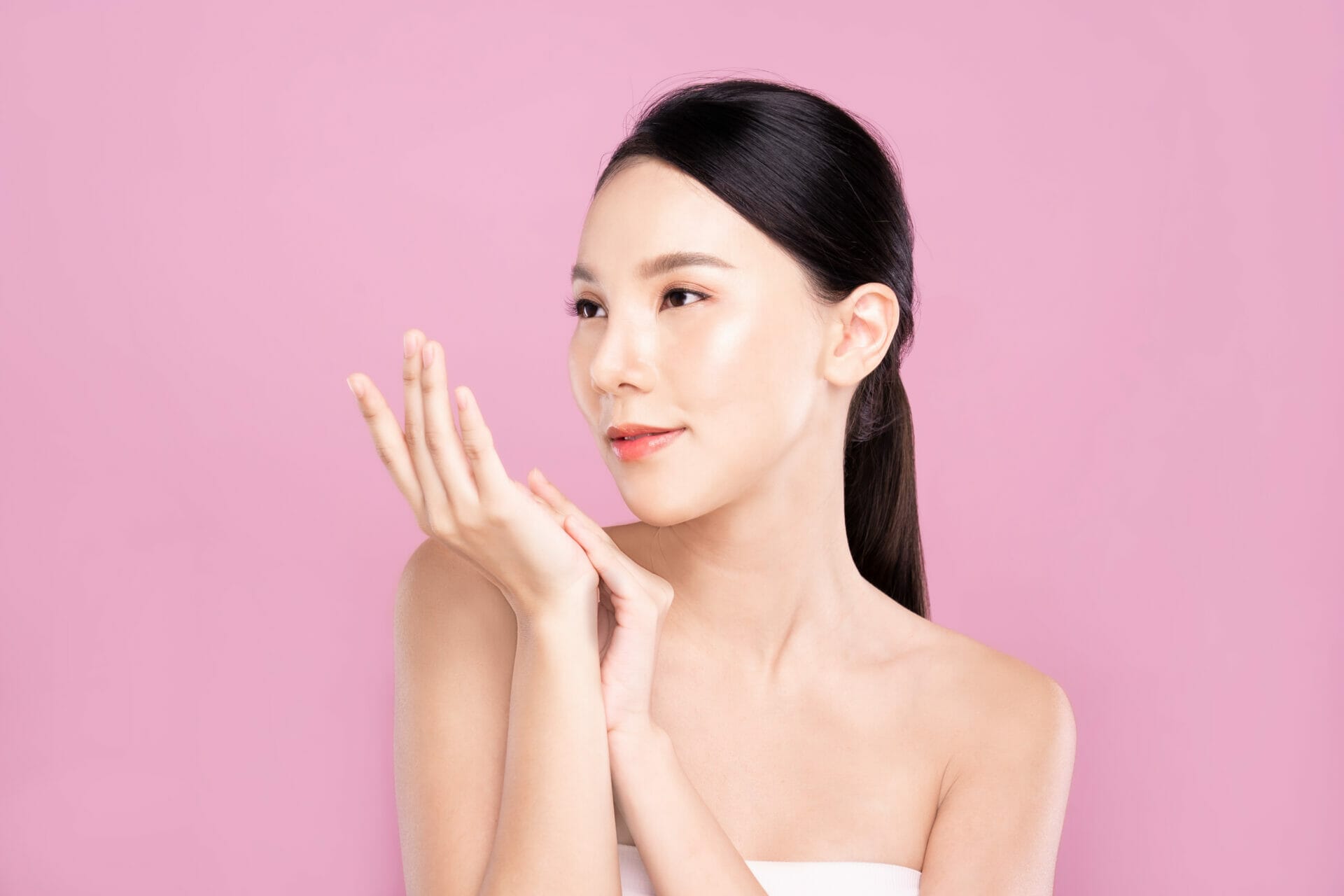 Beautiful Young Asian woman with clean fresh white skin touching hands softly in beauty pose. Girl smiling in isolated background. Facial treatment, cosmetic, make up and surgery advertisement